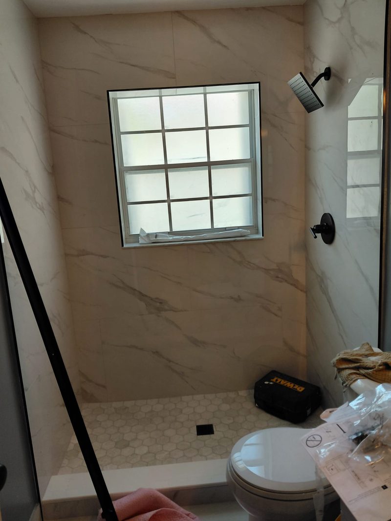 Marble-look tile shower with black fixtures and hex tile floor